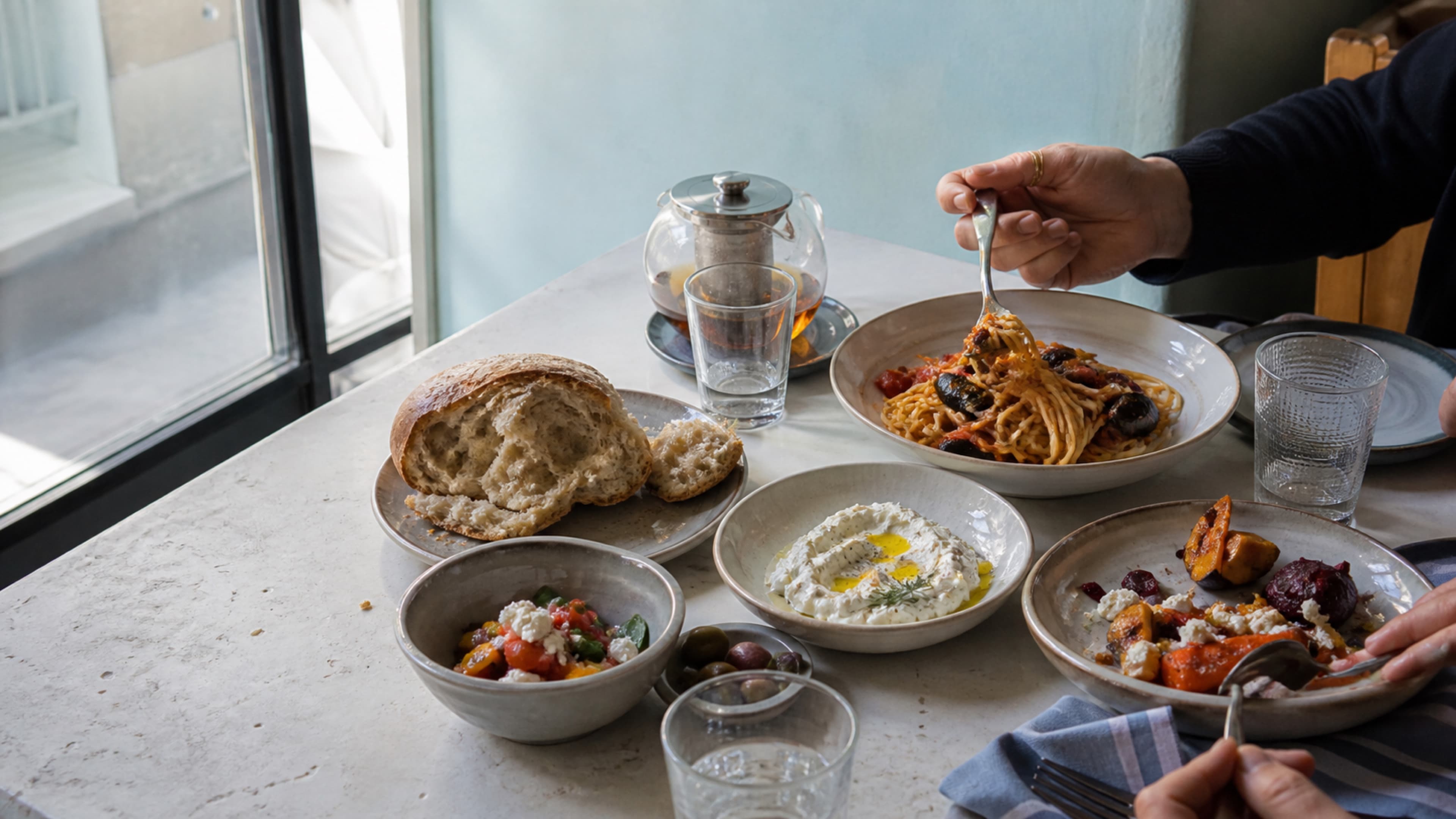 Pencere ışığında paylaşılan yemeklerle hazırlanmış bir restoran masası
